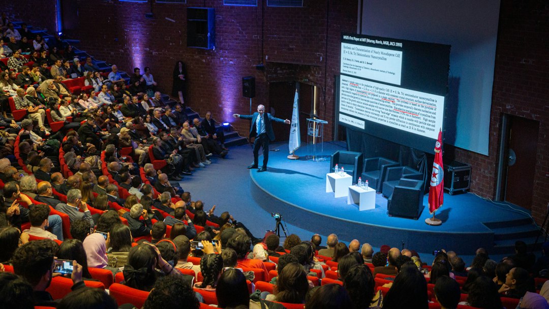 A speaker presenting to a large seated audience in an auditorium