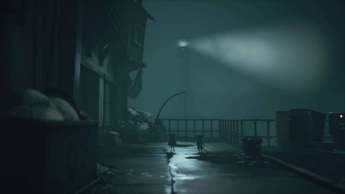 Two small figures on a foggy pier at night, with a lighthouse beam behind them, in Little Nightmares III - The Shores