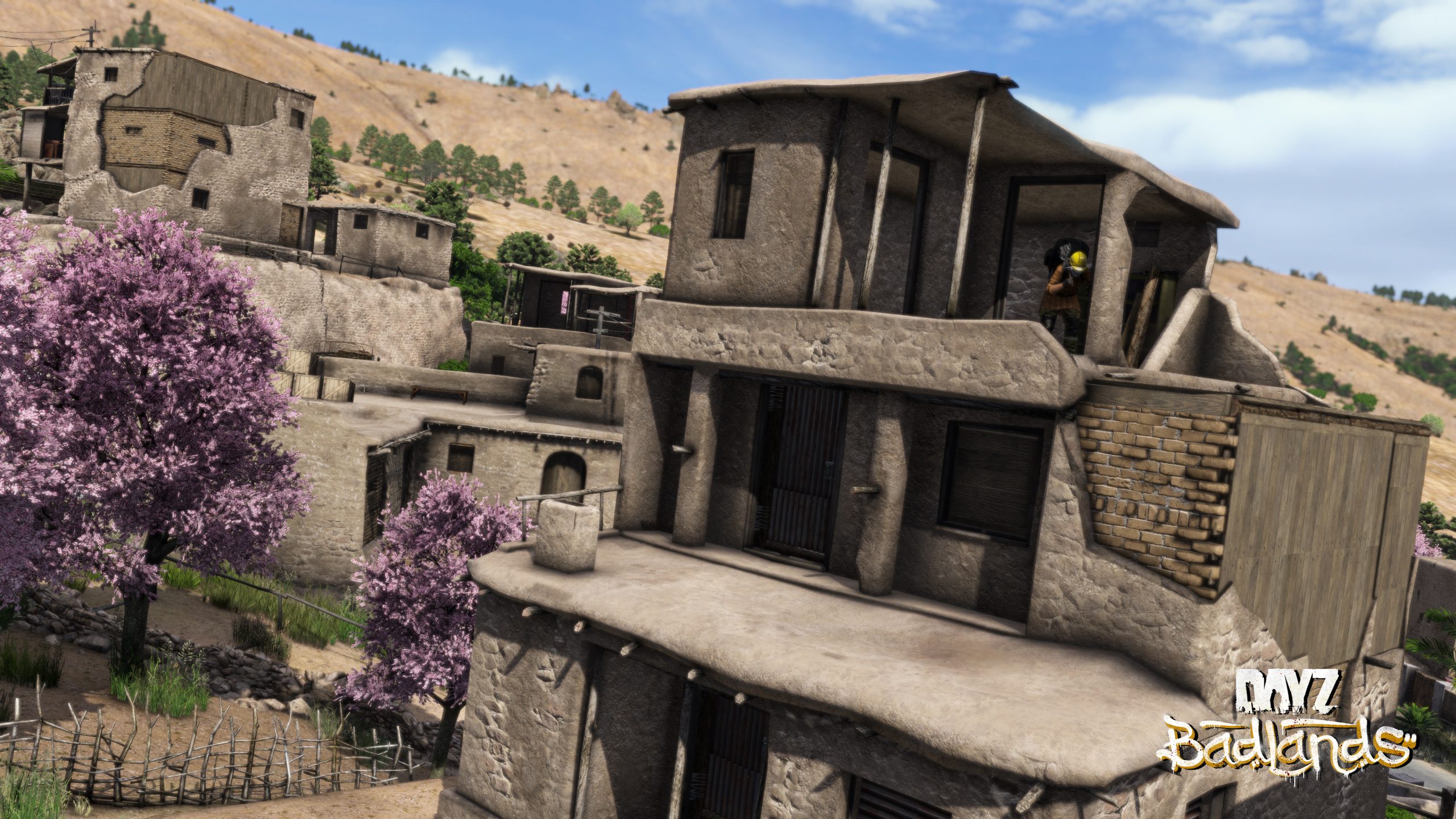 Stacked mud-brick buildings on a dry hillside beside two blossoming trees, with a player peering out of an upper window.