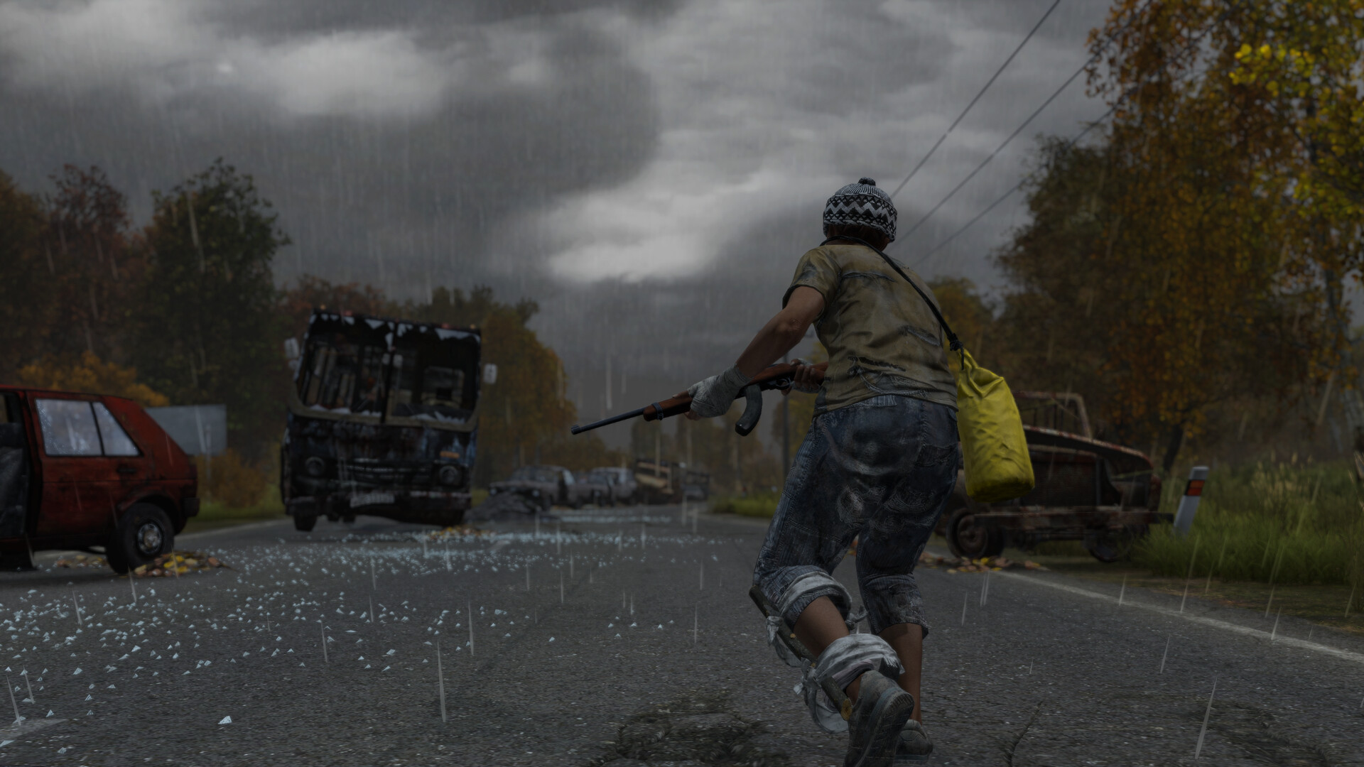 A DayZ survivor with a rifle and a yellow bag runs along a wet road past wrecked vehicles under a grey sky.