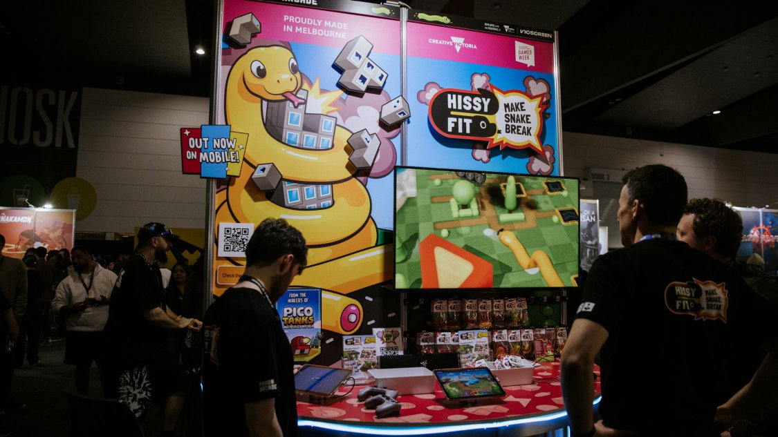 Visitors play at a colourful indie booth with a giant cartoon snake and a Proudly Made in Melbourne sign