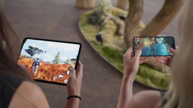 Two people play No Man's Sky with touch controls, one on an iPad and one on an iPhone