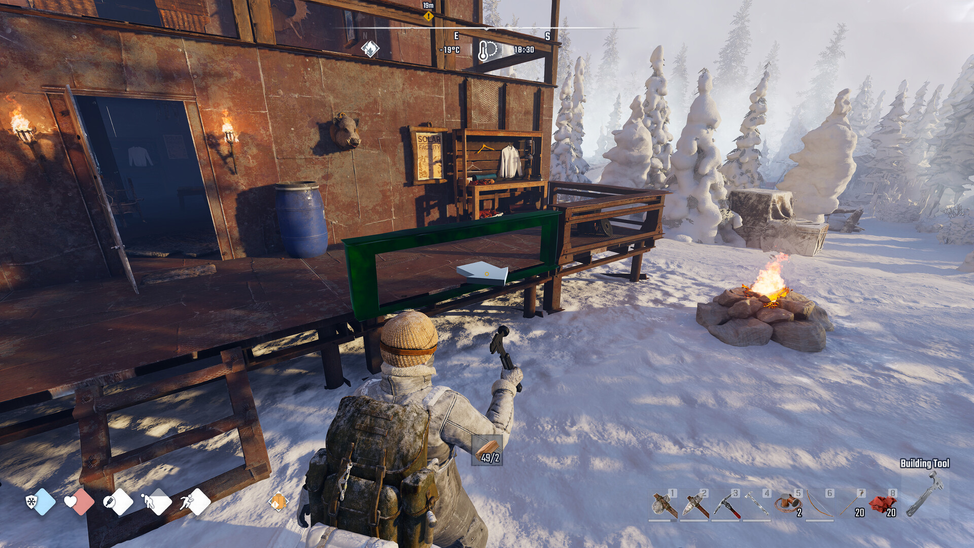 A survivor holding a hammer builds onto a timber shelter beside a campfire in the snow