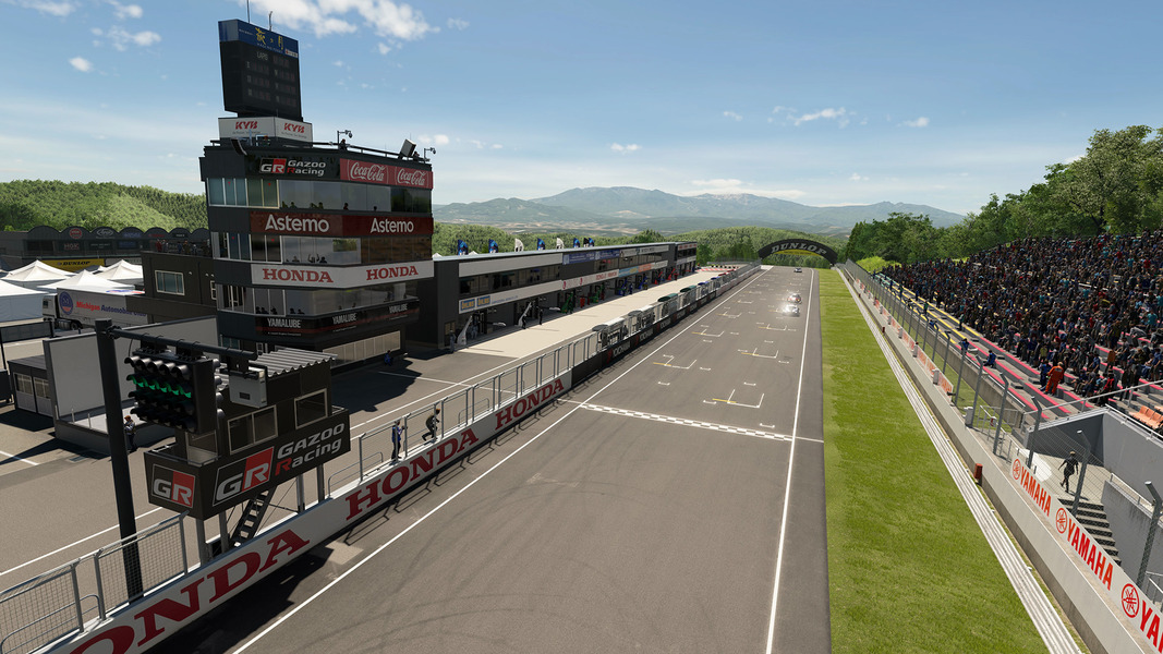 The main straight at Sportsland SUGO, with the control tower, pit buildings and green hills behind