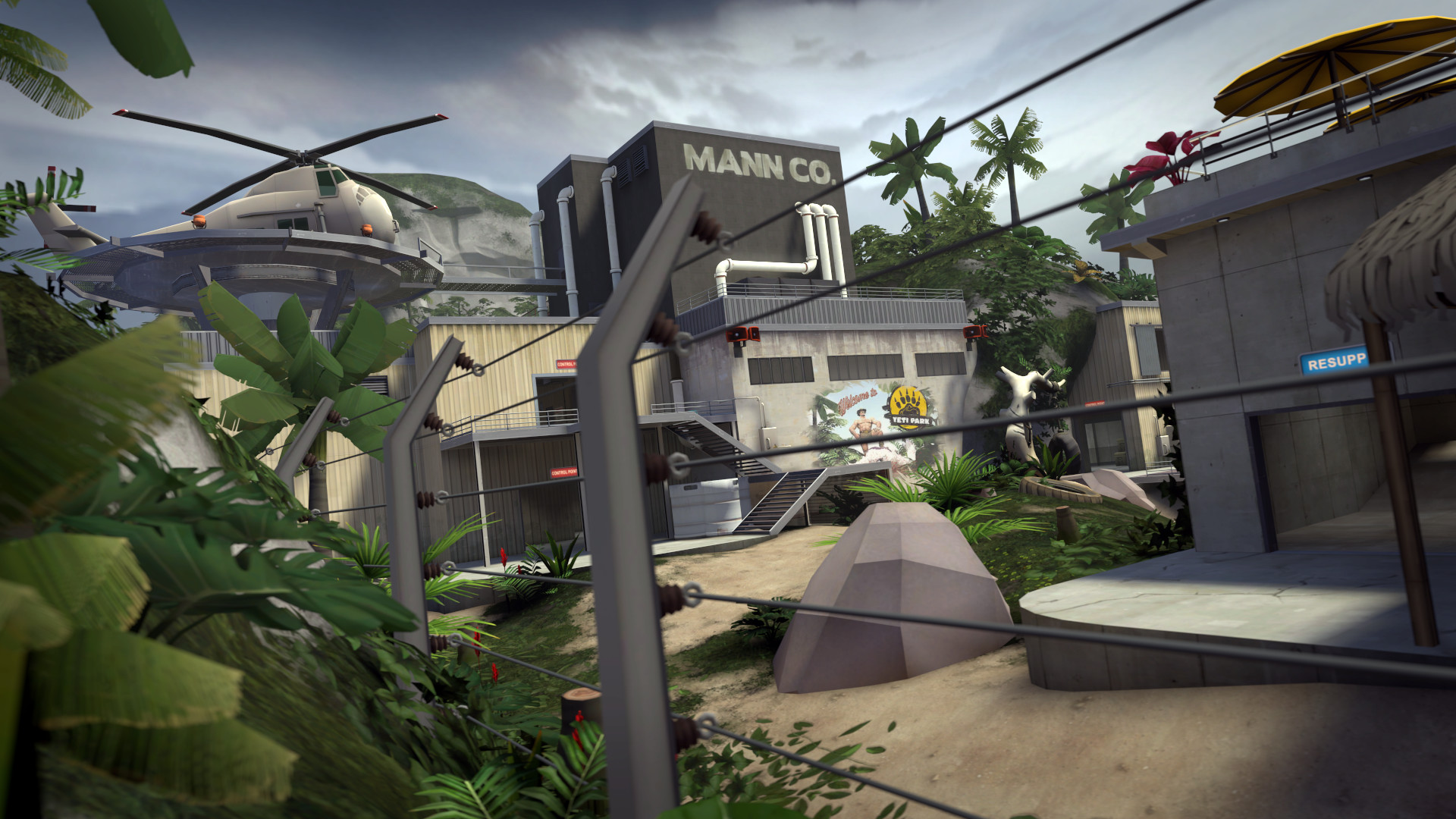 A tropical Team Fortress 2 map seen through a barbed fence, with a helicopter pad on the left and a Mann Co. building in the background