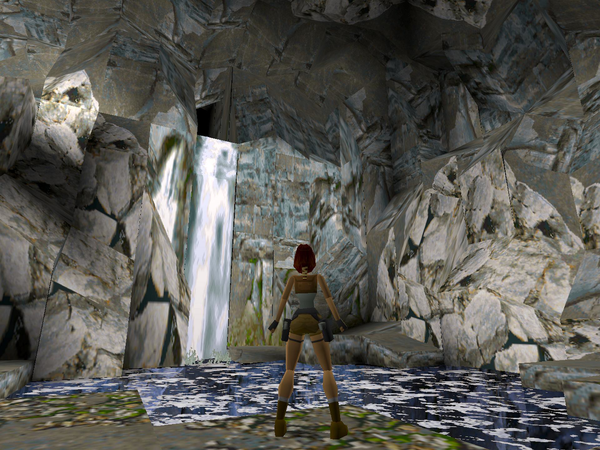 A screenshot from the original 1996 Tomb Raider showing the blocky polygon Lara Croft from behind, standing in a cave with a waterfall and jagged rock walls.