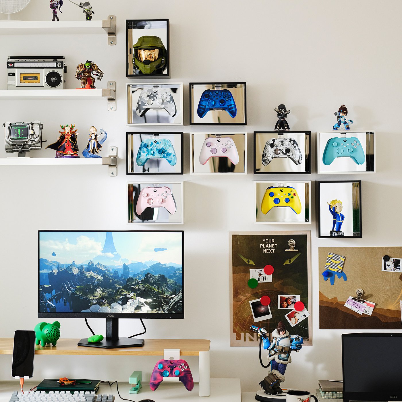 A wall of mirrored display boxes holding Xbox controllers and figurines, above a desk with a monitor